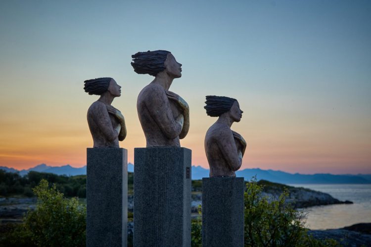 Side Shot of Statues of Three Women with Hands Folded Over Breasts and Sunrise in Background
